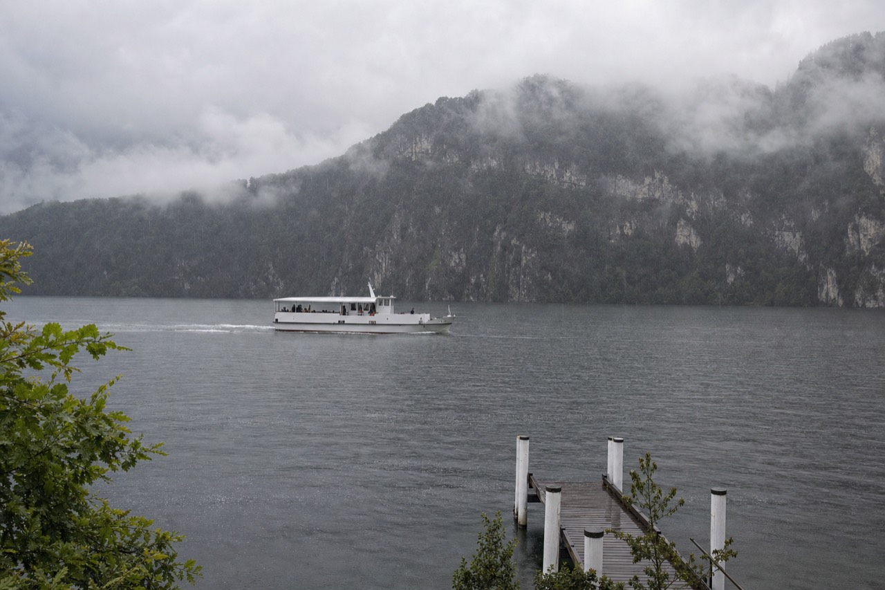 Rain clouds drifting over Lake Lucerne with green hills and calm water, no text, no logos, no people.