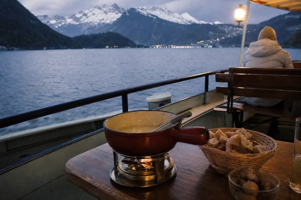 A fondue pot set on a wooden table on a boat's open deck on Lake Lucerne