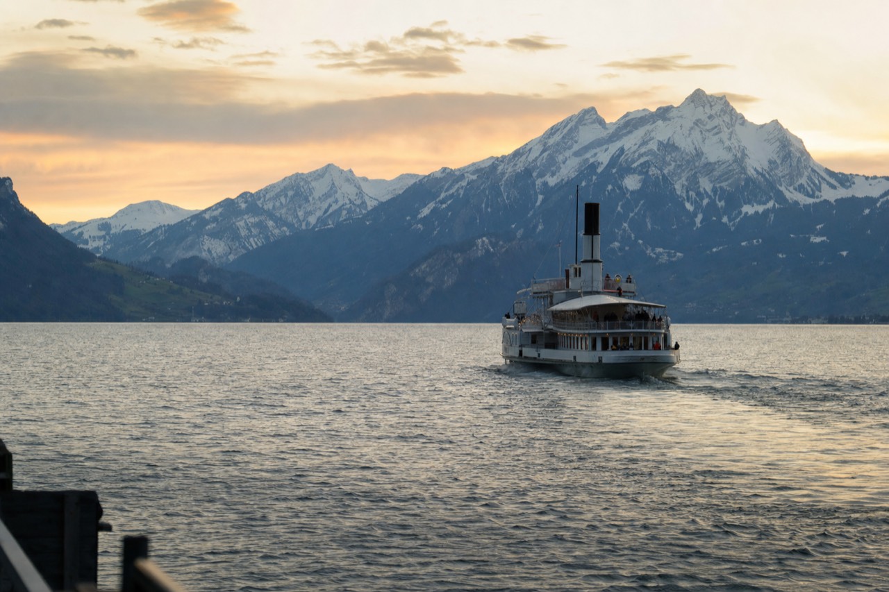 A historic paddle steamer crossing Lake Lucerne at golden hour with the Swiss Alps rising behind it